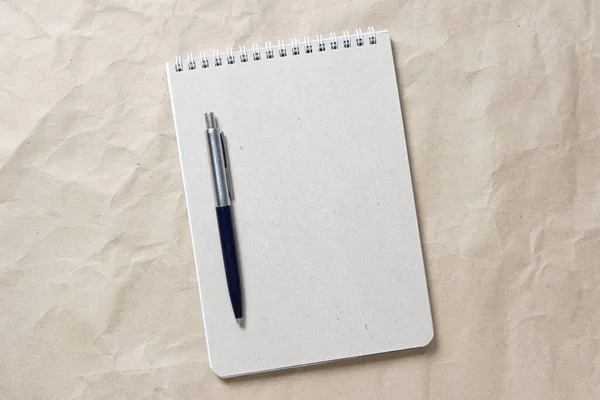 Szary notatnik z białą zwiniętą sprężyną i długopisem na tle beżowego pogniecionego papieru rzemieślniczego — Zdjęcie stockowe