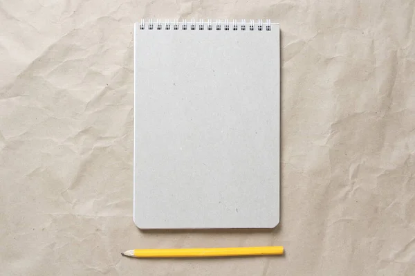 Blocco note grigio con molla bianca arrotolata e matita su uno sfondo di carta artigianale beige spiegazzata — Foto Stock