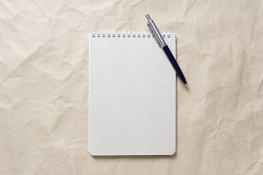  Beyaz sarmalanmış yay ve arkaplandaki bej buruşuk el işi kağıdının üzerindeki kalemle gri not defteri.