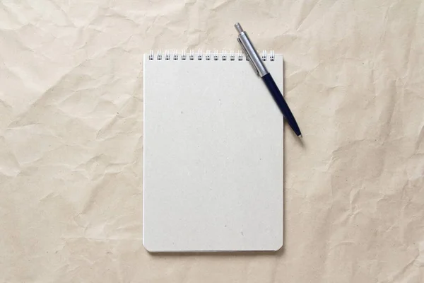 Gray notepad with white coiled spring and pen on a background of beige crumpled craft paper — Stock Photo, Image