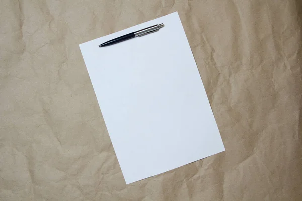 Feuille blanche vide de format A4 avec stylo sur un papier artisanal beige. — Photo