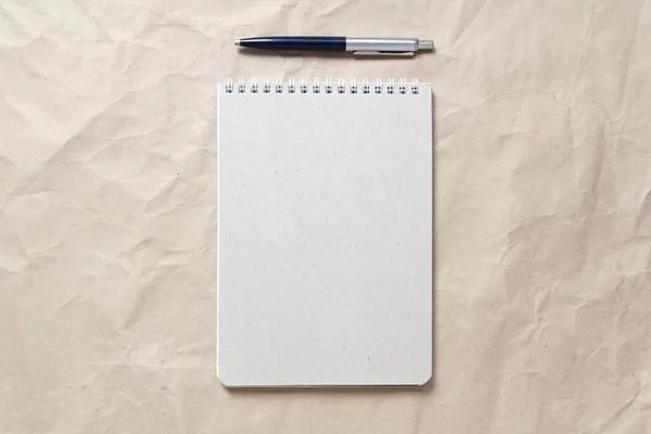 Gray notepad with white coiled spring and pen on a background of beige crumpled craft paper — Stock Photo, Image