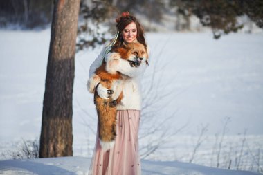 Güzel bir kız, karlı bir ormanda bir tilkiyle yürüyor. Soğuk hava. Kış Masalı. Kızıl Tilki. Peri masalı gibi fotoşop..
