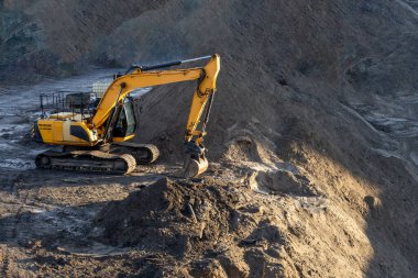 Kazıcı, minerallerin çıkarılması için toprak hareketinde çalışıyor. Kazıcı taş ocağında kum ve çakıl kazıyor. İnşaat alanında toprak çalışması sırasında ağır inşaat makineleri.