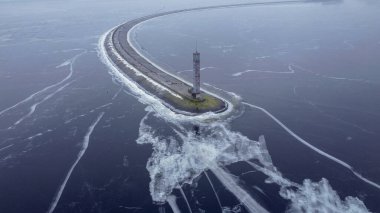 Buz çatlaklarında donmuş uzun bir barajın üzerinde bir deniz feneri. Hava görünümü