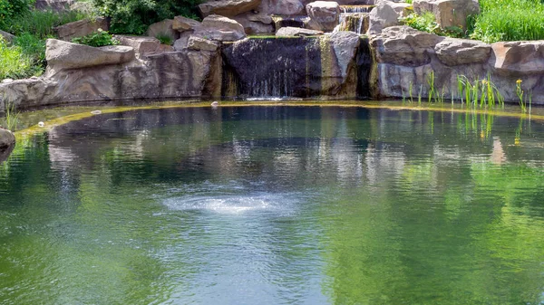 Yapay, küçük şelale kalıbının perspektif görüntüsü yosun suları ve akan su arkaplanı. Taşa seçici odaklanma.