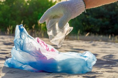 Dünyanın çevresel sorununda plastik kirliliği. Beyaz eldivenli bir el, çöpü plastik bir torbaya koyar. Kirlenmiş bölgelerdeki çöplerin çıkarılması ve temizlenmesi