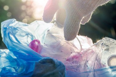 Dünyanın çevresel sorununda plastik kirliliği. Beyaz eldivenli bir el, çöpü plastik bir torbaya koyar. Kirlenmiş bölgelerdeki çöplerin çıkarılması ve temizlenmesi