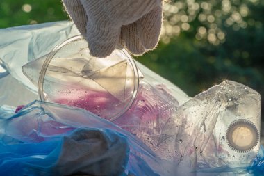 Dünyanın çevresel sorununda plastik kirliliği. Beyaz eldivenli bir el, çöpü plastik bir torbaya koyar. Kirlenmiş bölgelerdeki çöplerin çıkarılması ve temizlenmesi