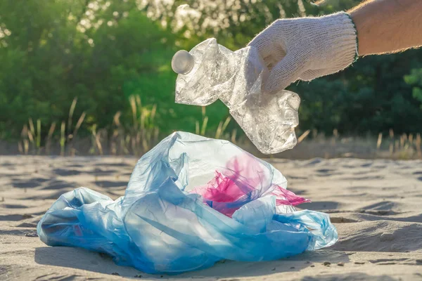 Plastic pollution in the environmental problem of the world. A hand in a white glove puts garbage in a plastic bag. Removal and cleaning of garbage from contaminated territories