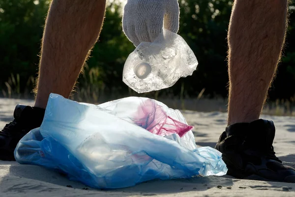 Plastic pollution in the environmental problem of the world. A hand in a white glove puts garbage in a plastic bag. Removal and cleaning of garbage from contaminated territories