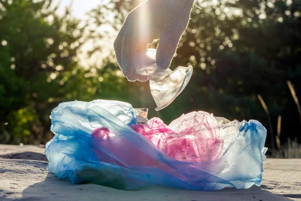 Plastic pollution in the environmental problem of the world. A hand in a white glove puts garbage in a plastic bag. Removal and cleaning of garbage from contaminated territories