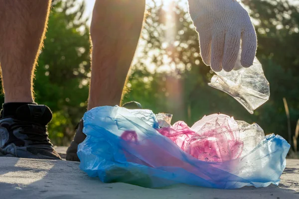 Plastic pollution in the environmental problem of the world. A hand in a white glove puts garbage in a plastic bag. Removal and cleaning of garbage from contaminated territories