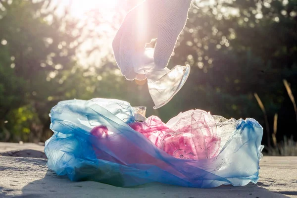 Plastic pollution in the environmental problem of the world. A hand in a white glove puts garbage in a plastic bag. Removal and cleaning of garbage from contaminated territories