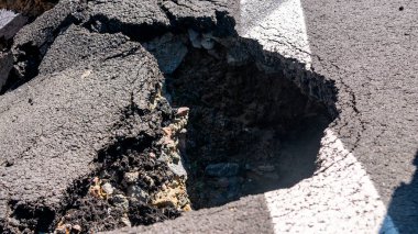 Dangerous stretch of road with damaged asphalt. The accident site is fenced off with black and yellow tape. The concept of repair or accident of sewerage, underground communications, water supply.