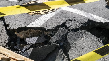 Dangerous stretch of road with damaged asphalt. The accident site is fenced off with black and yellow tape. The concept of repair or accident of sewerage, underground communications, water supply.
