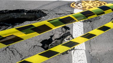Dangerous stretch of road with damaged asphalt. The accident site is fenced off with black and yellow tape. The concept of repair or accident of sewerage, underground communications, water supply.