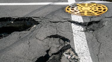 Dangerous stretch of road with damaged asphalt. The accident site is fenced off with black and yellow tape. The concept of repair or accident of sewerage, underground communications, water supply.