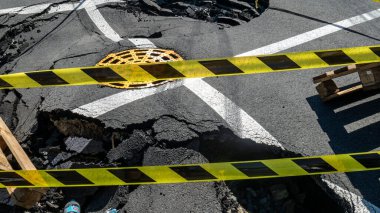Dangerous stretch of road with damaged asphalt. The accident site is fenced off with black and yellow tape. The concept of repair or accident of sewerage, underground communications, water supply.