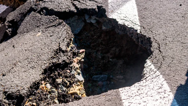 Dangerous stretch of road with damaged asphalt. The accident site is fenced off with black and yellow tape. The concept of repair or accident of sewerage, underground communications, water supply.