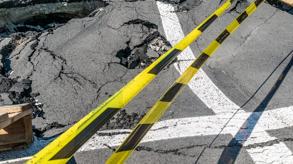 Dangerous stretch of road with damaged asphalt. The accident site is fenced off with black and yellow tape. The concept of repair or accident of sewerage, underground communications, water supply.