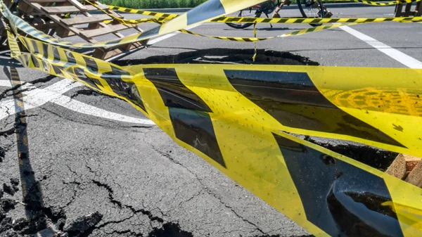 Dangerous stretch of road with damaged asphalt. The accident site is fenced off with black and yellow tape. The concept of repair or accident of sewerage, underground communications, water supply.
