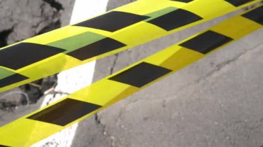 Dangerous stretch of road with damaged asphalt. The accident site is fenced off with black and yellow tape. The concept of repair or accident of sewerage, underground communications, water supply.