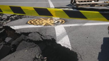 Dangerous stretch of road with damaged asphalt. The accident site is fenced off with black and yellow tape. The concept of repair or accident of sewerage, underground communications, water supply.