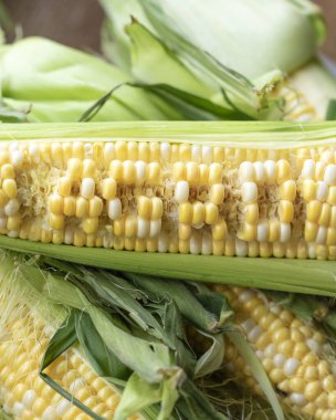Raw cobs of young corn with leaves on a wooden table. the inscription on the cob 