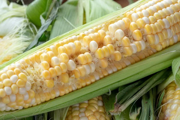 Raw cobs of young corn with leaves on a wooden table. the inscription on the cob \