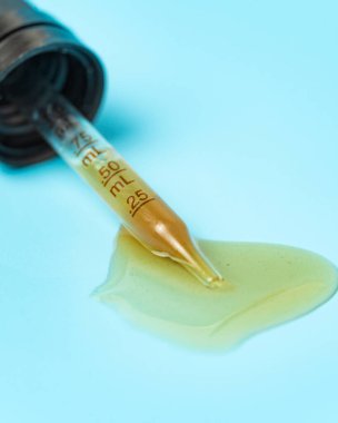 Tıbbi ve kozmetik amaçlar için kullanılan mavi zemin üzerine dökülmüş sarı sıvıyla bir boru.