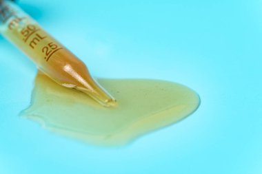 Tıbbi ve kozmetik amaçlar için kullanılan mavi zemin üzerine dökülmüş sarı sıvıyla bir boru.