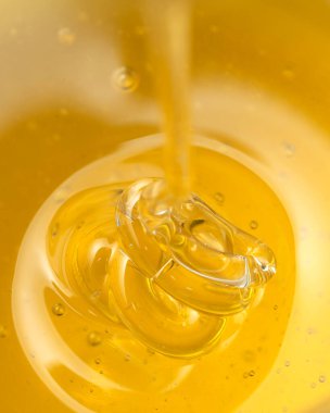 Bal, sarı arka plandaki ahşap bir baldan damlıyor. Tasarımınız için tatlı arı ürünü. Yakın plan.