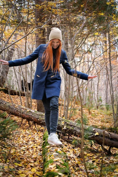 Happy young red haired woman smiling and balancing on a log. walking in an autumn forest. local travel. spending time in an old park, relaxing and having fun. — Stock Photo, Image