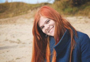 Mavi ceketli, gülümseyen kızıl saçlı genç bir kadın ve seyirciye bakıyor. Mutlu kızıl saçlı kadının sonbahar portresi