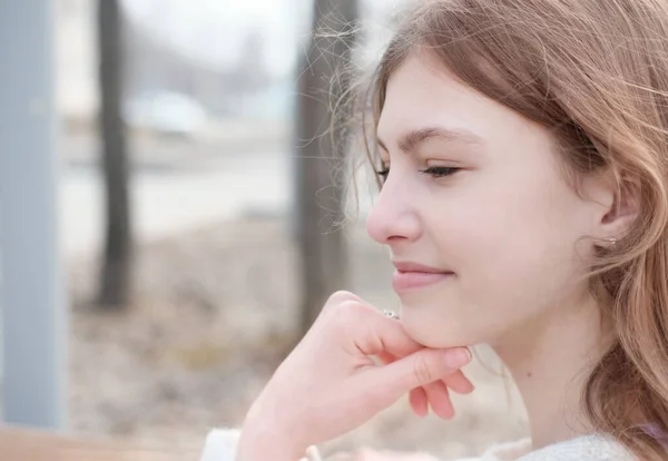 Pretty teenager girl with long brown hair looking aside and touching her chin. outdoor portrait of beautiful teenager girl. — Stock Photo, Image