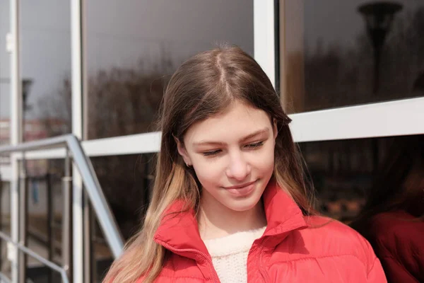 Szczęśliwa uśmiechnięta nastolatka w zimowej kurtce stojąca przy ścianie okna. uliczny portret pięknej nastolatki patrząc na bok. — Zdjęcie stockowe