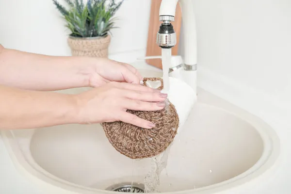 Crop view woman washing the dishes with natural zero waste sponge made og jute. hand made eco kitchen accsessories. blond middle age woman cleaning up in a modern kitchen Royalty Free Stock Photos