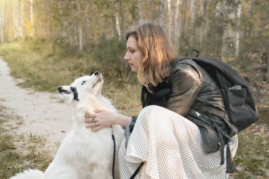 Yakutian laika köpeğinin sahibinin yanında oturup sevgi ve ilginin tadını çıkarması. Kadın okşuyor ve köpeğine bakıyor. Evcil bir arkadaş, ormanda evcil hayvanlarla yürüyor.
