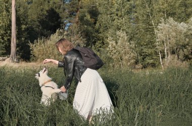Nehir kıyısında oynayıp köpeğini eğiten mutlu beyaz kadın. Komik Yakutian laykası atlıyor ve ödül yakalamaya çalışıyor..