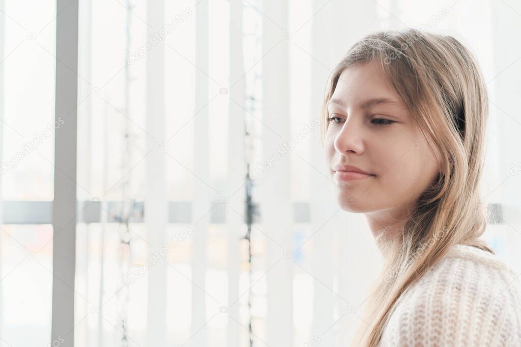calm and peaceful teenager girl sitting in front of a window. beautiful girl looking aside and thinking. inner peace, mind health and balance for teens.