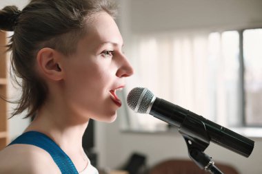 Genç duygusal kadın mikrofona şarkı söylüyor. Plak stüdyosunda prova yapan bayan bir rock şarkıcısı. yan görünüm