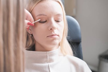 Makyaj sanatçısı makyaj malzemeleriyle düzeltmeler yapıyor. Güzellik salonunda gözleri kapalı, göz farı süren bir kadın model..