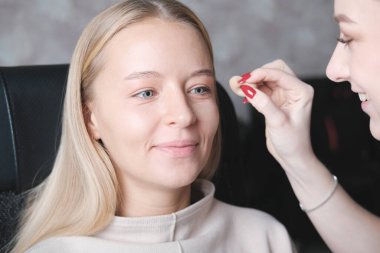 Bir müşteri için profesyonel makyaj yaparken gülümseyen genç bir vize. Güzellik salonunda sarışın, mutlu bir kadın. küçük işletme.