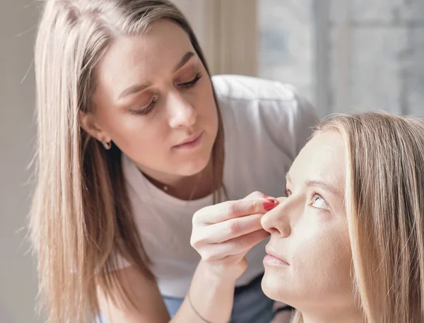 Makyaj sanatçısı güzellik salonundaki gelinin ten rengini düzeltiyor. Genç bayan müşteri ve vizeci.