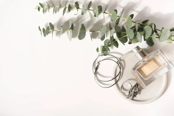Butelka perfum i kobieca biżuteria na szarym betonowym talerzu i gałązka eukaliptusa na białym stole. akcesoria dla kobiety. luksusowy styl życia. treści blogerów — Zdjęcie stockowe