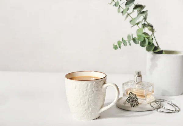 Una taza de café y accesorios femeninos en una mesa. una botella de perfume y joyas y hojas verdes sobre una mesa blanca. buen concepto de mañana. —  Fotos de Stock