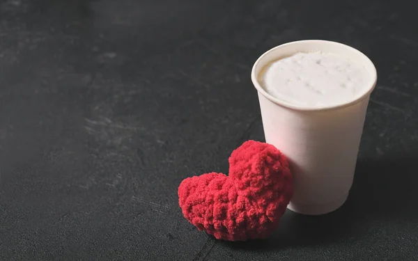 Kartónový šálek kávy se šlehačkou a pleteným červeným srdcem na černém pozadí. kopírovat prostor. Káva s sebou. Valentýn a koncept lásky. — Stock fotografie
