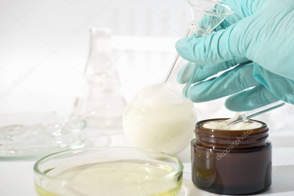 hand in rubber medical glove holding laboratory glassware with fermented cosmetic product, face cream with enzymes developed in a lab