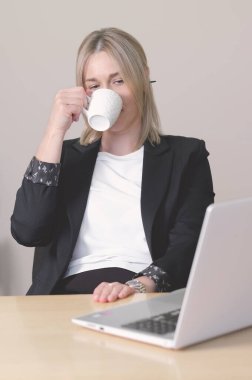 Resmi takım elbiseli bir kadın dizüstü bilgisayarla masada oturuyor ve kahve içiyor. Günün ortasında ara vermek gibi bir şey. Zor bir gün, çok çalışmak. dikey çekim.